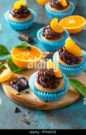 Orange Cupcakes mit Schokolade und Sahne frische Mandarinen auf einem blauen Stein oder Beton. Stockfoto