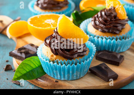 Orange Cupcakes mit Schokolade und Sahne frische Tangerinen close-up auf einem blauen Stein oder Beton. Stockfoto