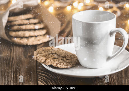 Kaffee Tasse auf einem Teller mit hausgemachten Haferflocken Cookies, Backen auf Holz rustikal Tisch, serviert mit Winter Zubehör. Winterurlaub noch leben Weihnachten o Stockfoto