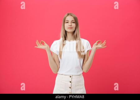 Blond schönes Junge weibliche Macht mudra Zeichen, entspannt nach einem harten Arbeitstag, hält die Augen geschlossen, übt Yoga gegen Rosa Hintergrund. Junge hübsche Frau meditiert, Indoor. Entspannung Konzept. Stockfoto