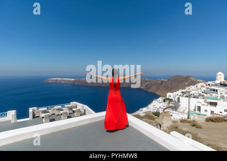 Eine Frau in einem roten Kleid genießen die Imerovigli auf Santorin Kykladen Griechenland Aussicht auf einen sonnigen Sommer am Nachmittag Stockfoto