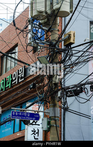 Eine hölzerne Stange hält Strom und Kommunikation Kabel, die kreuz und quer über die Straße in Haeundae, Busan, Südkorea. Stockfoto