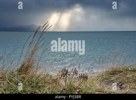 Sonnenstrahlen brechen durch schwere Gewitterwolken über dem Meer auf einem Strand in Südostalaska. Stockfoto