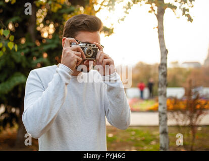 Junge schöne hipster Kerl geht in einem schönen Herbst Park auf dem Hintergrund der gelben Blätter in warmen und sonnigen Wetter und nimmt Bilder auf einem Schwein film Stockfoto