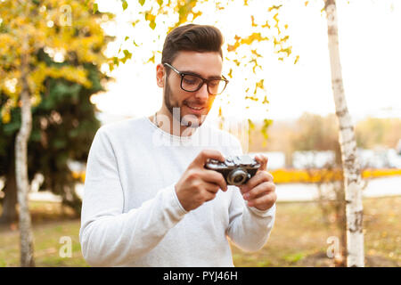 Junge schöne hipster Kerl geht in einem schönen Herbst Park auf dem Hintergrund der gelben Blätter in warmen und sonnigen Wetter und nimmt Bilder auf einem Schwein film Stockfoto