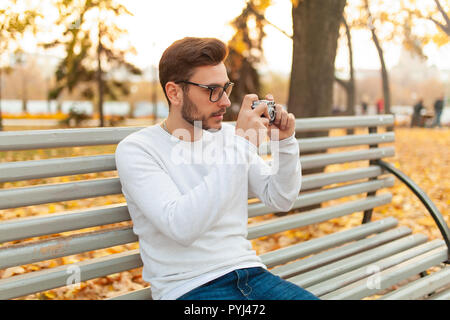 Junge schöne hipster Kerl geht in einem schönen Herbst Park auf dem Hintergrund der gelben Blätter in warmen und sonnigen Wetter und nimmt Bilder auf einem Schwein film Stockfoto