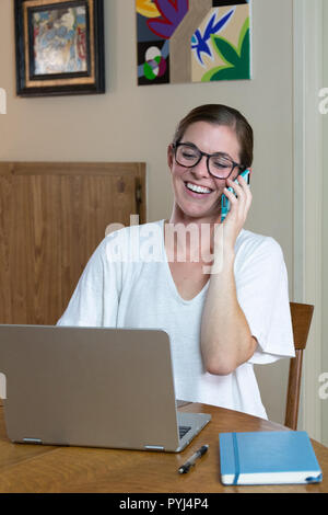 Junge brünette Frau Künstler und Maler Arbeiten am Computer am Esstisch Gespräch am Handy lachen. Stockfoto