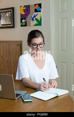 Junge Frau Künstler in Journal mit Handy und Laptop verbunden bleiben, während die von zu Hause aus arbeiten schreiben. Stockfoto
