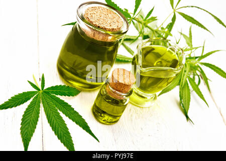 Hanf Öl in zwei Gläsern und sauceboat, Blätter und Stängel von Cannabis auf dem Hintergrund der Holzbretter Stockfoto
