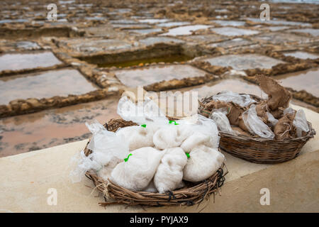 Salinas. Salinen oder salters im Hintergrund mit Salz Beutel zum Verkauf bereit in einem Korb oder Schüssel outdoor. Hand Ernte Salz in Insel Gozo Marsalforn Stockfoto