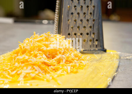 Stapel von geriebenem Käse neben einem metallreibebrett in der Küche Stockfoto