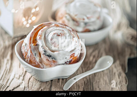 Leckere hausgemachte süße Brötchen mit Zimt und Puderzucker Weihnachten im alten Holztisch. Traditionelle schwedische Gebäck, kanelbullar. Stockfoto