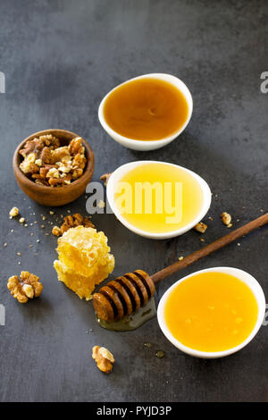 Natürliche verschiedene Honig und Nüssen. Honig im Glas und Pendelarm, Süße Waben auf dunklen Tisch aus Stein. Stockfoto