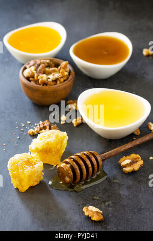 Natürliche verschiedene Honig und Nüssen. Honig im Glas und Pendelarm, Süße Waben auf dunklen Tisch aus Stein. Stockfoto