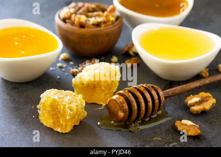 Natürliche verschiedene Honig und Nüssen. Honig im Glas und Pendelarm, Süße Waben auf dunklen Tisch aus Stein. Stockfoto