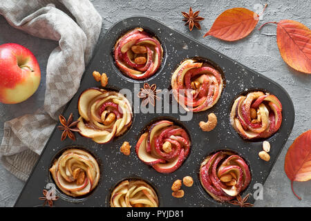 Fach von Apple Rosen in Blätterteig gebacken auf grauem Beton Hintergrund mit Herbstlaub und rote Äpfel Stockfoto