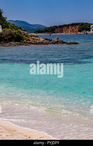 Feder tagsüber schönen Ionischen Meer mit klaren türkisfarbenen Wasser, Felsen und Bäume Küste Blick von Ksamil Strand, Albanien. Deep Blue Sky Stockfoto