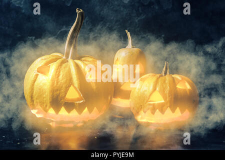 Scary Halloween Kürbisse auf einem schwarzen Hintergrund. Unheimlich glühenden Gesichtern Trick oder mit Dunst und Nebel behandeln Stockfoto