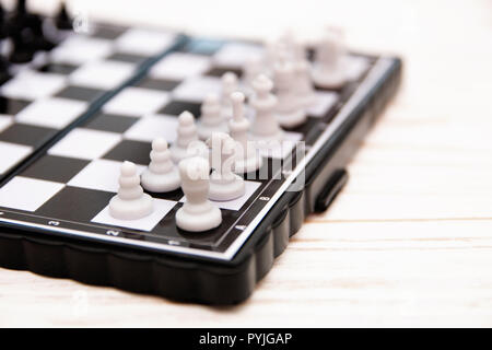 Kleine Schach, Kunststoff Schachfiguren auf einem Schachbrett, auf ein weißes Holz- Hintergrund Stockfoto