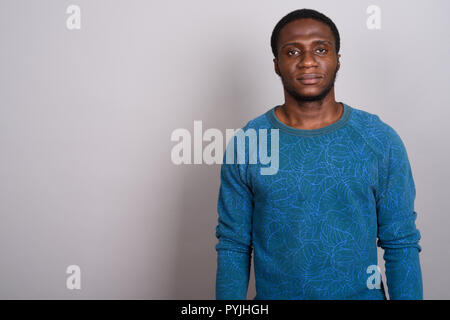 Junge afrikanische Mann trägt blaue Langarm Shirt gegen Grau b Stockfoto