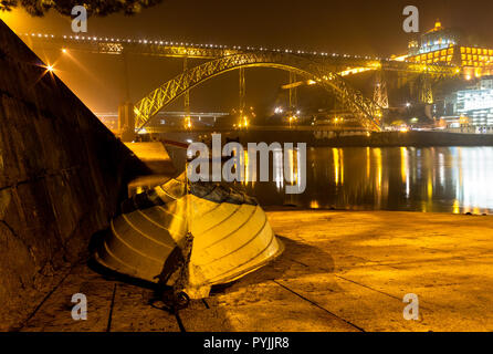 Ein Boot sitzt in der Nähe des Flusses Douro in Porto in der Nacht mit dem Luis Brücke im Hintergrund. Stockfoto