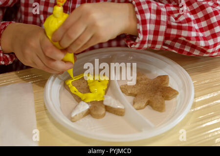 Junge in einer Plaid Shirt verziert mit gelben Creme die Kekse in der Form eines Engel und ein Star Stockfoto