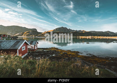 Traditionelles rotes fishin Haus in der Nähe von Reine Bjoernsand auf den Lofoten, Norwegen mit roten rorbu Häuser. Am Nachmittag den Sonnenuntergang mit Wolken an einem Sandstrand. Foto t Stockfoto