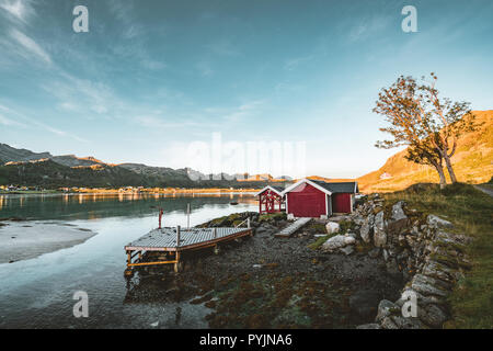 Traditionelles rotes fishin Haus in der Nähe von Reine Bjoernsand auf den Lofoten, Norwegen mit roten rorbu Häuser. Am Nachmittag den Sonnenuntergang mit Wolken an einem Sandstrand. Foto t Stockfoto