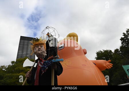 New York, USA 28. Oktober 2018. Ein Mann in einem Trumpf Maske steht vor einem 20 Fuß hohen Ballon, Präsident Trumpf als Baby in Windeln bei einer Rallye von Demonstranten im Battery Park, der die Amtsenthebung von Trumpf. Die Demonstranten haben ähnliche Ballons in anderen anti-Trumpf-Proteste in den USA und Großbritannien die Rallye und März von einer Gruppe von Menschen, die beschuldigt die Präsidenten der Hohen begehen Verbrechen und Vergehen genannt organisiert wurde. Credit: Joseph Reid/Alamy leben Nachrichten Stockfoto