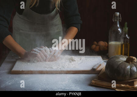 Hände kneten den Teig von Frauen. Backzutaten auf hölzernen Tisch Kürbis Milch Öl Mehl Stockfoto