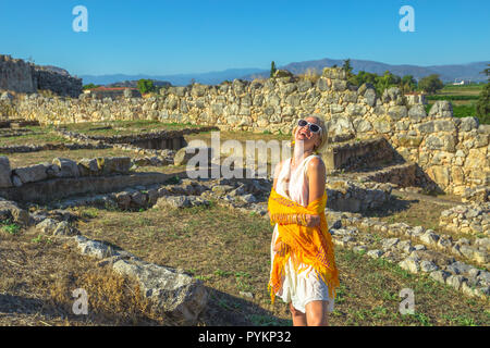 Schöne touristische Frau in griechischen Dress lächelte spitzbübisch am historischen Ort in Griechenland. Frau beliebte alte Mykene in einen schönen Tag. Europa Weltkulturerbe. Stockfoto