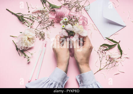 Weibliche Hände, schöne Blumen Anordnung mit Pfingstrosen Blumen auf Pastell rosa Hintergrund mit Umschlag, Ansicht von oben Stockfoto