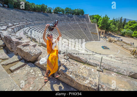 Reisen Fotograf unter selfie mit Spiegelreflexkamera. Frau sitzt auf der Treppe von Epidaurus Theater, nimmt Bilder in archäologischen Stätte, Peloponnes, Griechenland. Sommer Urlaub Lifestyle. Stockfoto