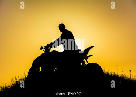 Silhouette der Quad Bike Fahrer auf dem Berg/Силует квадроциклиста на свете закатном горе в Stockfoto