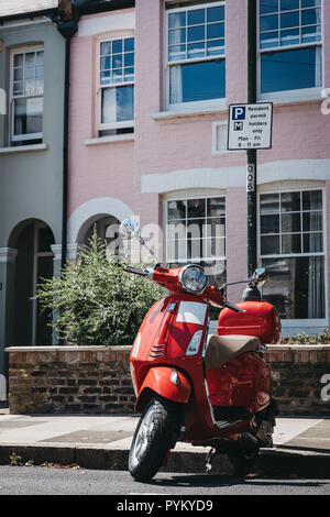 London, Großbritannien - 1 August 2018: Rote Vespa Motorrad durch ein Haus in Barnes, London geparkt. Vespa ist eine berühmte italienische Marke von Scooter hergestellt von Piagg Stockfoto