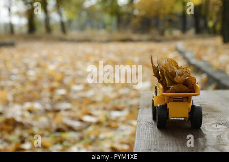 Das Konzept der saisonalen Ernte im Herbst Laub ist in der Form eines Spielzeugs gelbe Lastwagen geladen mit Blättern vor dem Hintergrund der Dargestellten Stockfoto