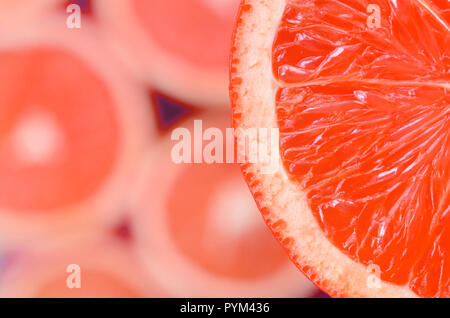 Blick von oben auf ein Fragment des Roten grapefruit Slice auf dem Hintergrund der vielen unscharfen Grapefruit Schichten. Ein citrus Textur Bild gesättigt Stockfoto