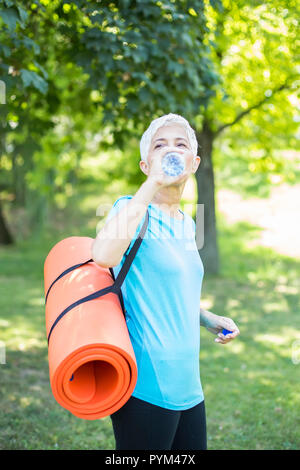 Portrait der älteren Frau hält Fitness Matte auf ihr zurück in den Park und die Vorbereitung der Übung Stockfoto