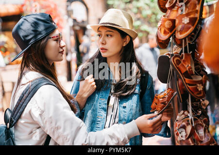 Hübsche Frauen an der niedlichen Leder Schuhe für Ihre Kinder auf dem Markt suchen. Happy Travel zusammen von zwei Mädchen mit Hut in der sonnigen Stadt. Gruppe von ha Stockfoto