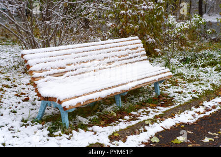 Herbstlandschaft: Alte Gartenbank im Spätherbst der erste Schnee bedeckt. Schießen im Oktober Stockfoto