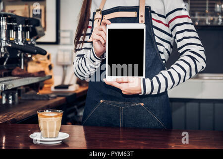 Asiatische Frau barista Schürze tragen Jean Holding leerer Bildschirm Tablet für Kunden an Theke mit Smile Emotion, Cafe Restaurant Service Konzept, Inhaber sm Stockfoto