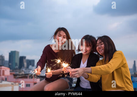 Happy Gruppe von asiatischen Mädchen Freunde genießen und wunderkerze am Dach Party spielen am Abend Sonnenuntergang, Urlaub Feier festlich, Teenager Lebensstil, Freiheit ein Stockfoto