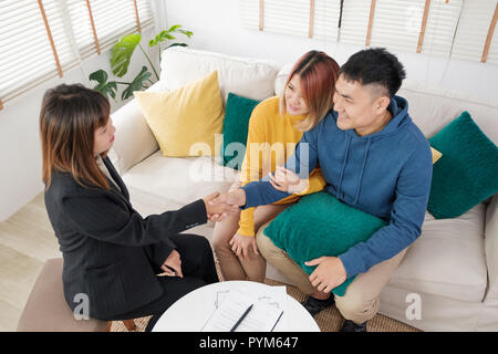 Asiatische Paar home Vertrag und Handshake mit Realtor im Wohnzimmer im neuen Zuhause. Kauf neues Haus Immobilien Stockfoto