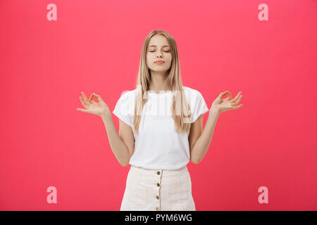 Blond schönes Junge weibliche Macht mudra Zeichen, entspannt nach einem harten Arbeitstag, hält die Augen geschlossen, übt Yoga gegen Rosa Hintergrund. Junge hübsche Frau meditiert, Indoor. Entspannung Konzept. Stockfoto