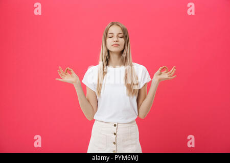 Blond schönes Junge weibliche Macht mudra Zeichen, entspannt nach einem harten Arbeitstag, hält die Augen geschlossen, übt Yoga gegen Rosa Hintergrund. Junge hübsche w Stockfoto