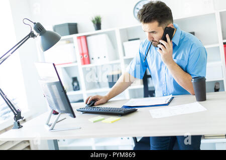 Ein junger Mann, der im Büro am Computer und am Telefon zu sprechen. Stockfoto