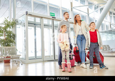 Eltern und zwei Kinder mit Gepäck im Flughafen Terminal freuen sich auf einen Urlaub mit der ganzen Familie Stockfoto