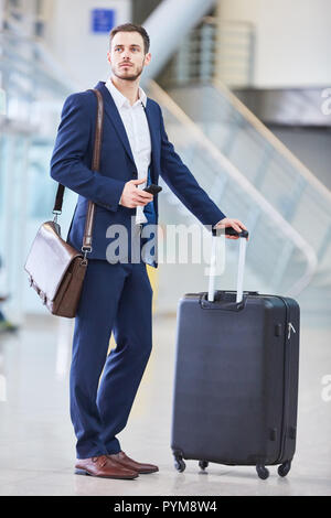 Junge Geschäftsmann mit Trolley und Smartphone im Flughafen Terminal am Zwischenstopp Stockfoto