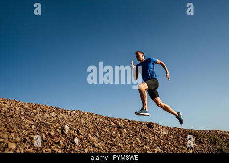 Dynamische läuft bergauf Athlet runner auf dem Hintergrund des blauen Himmels Stockfoto