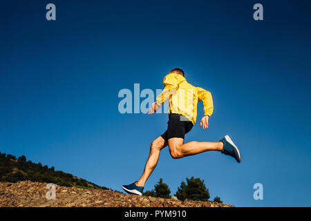 Männliche Athlet Läufer in gelber Jacke laufen bergauf Stockfoto